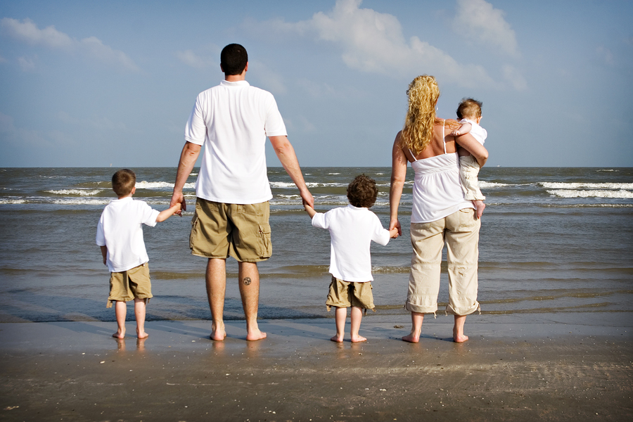 A man and woman co-parenting holding their children's hands on a beach